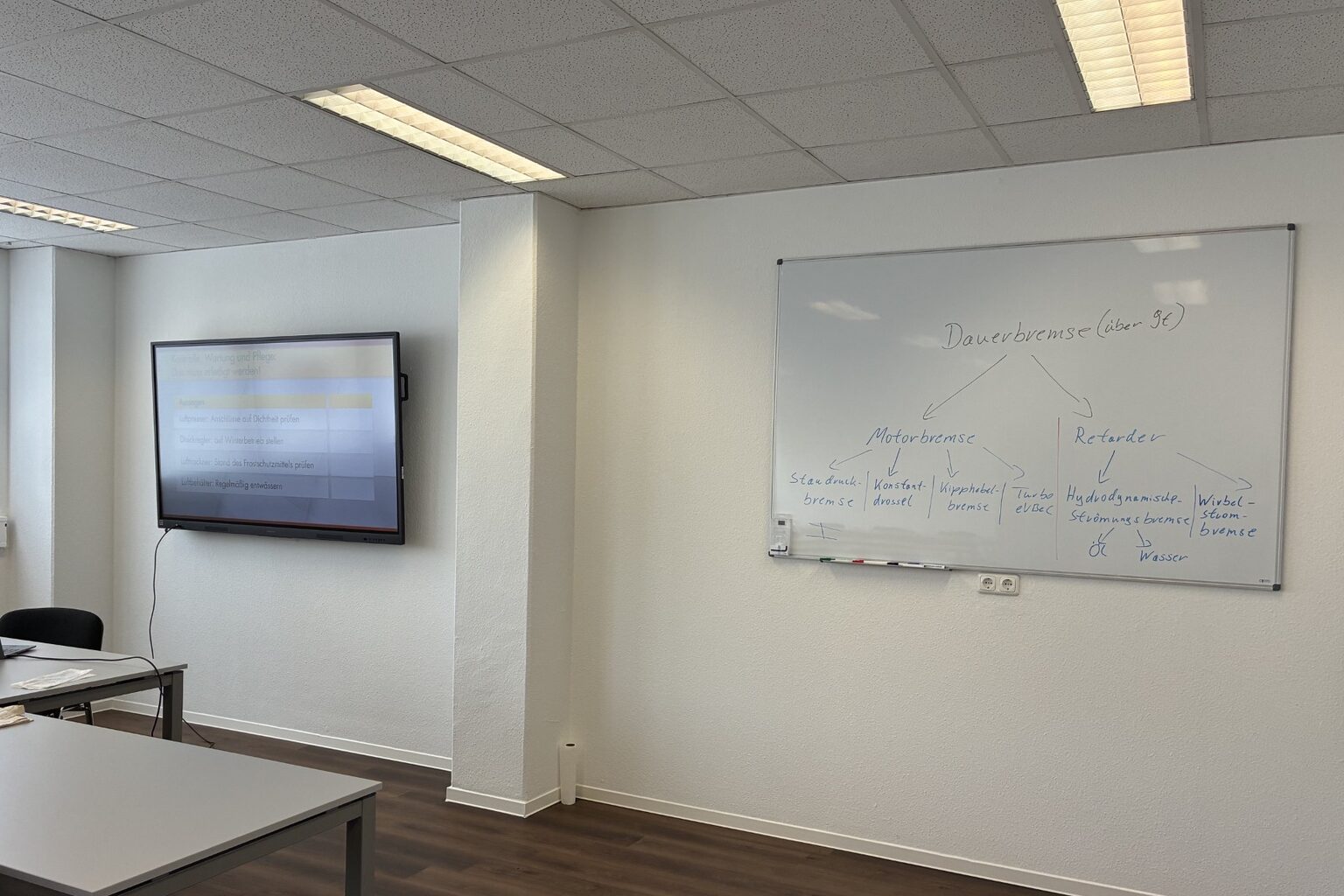 Leerer Schulungsraum mit Tischen, einem Bildschirm an der Wand und einem beschriebenen Whiteboard
